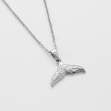 Silver whale tail pendant on a chain against a light gray background