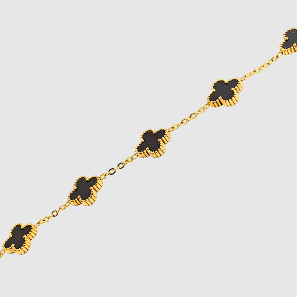 Gold chain bracelet with black clover-shaped charms on a white background