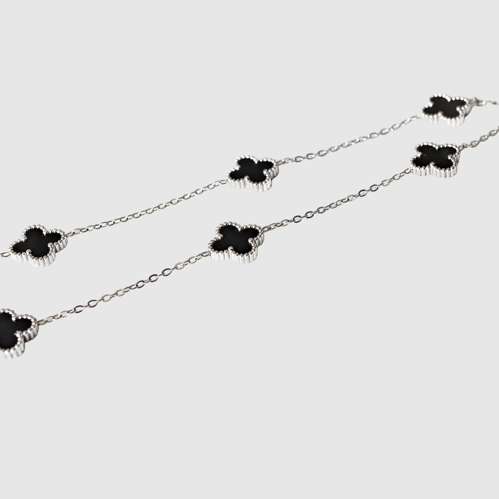 Silver necklace with black clover-shaped pendants on a white background
