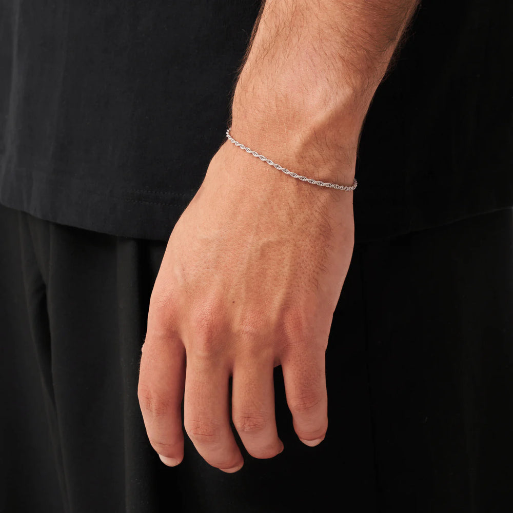 Hand wearing a silver bracelet on a black background