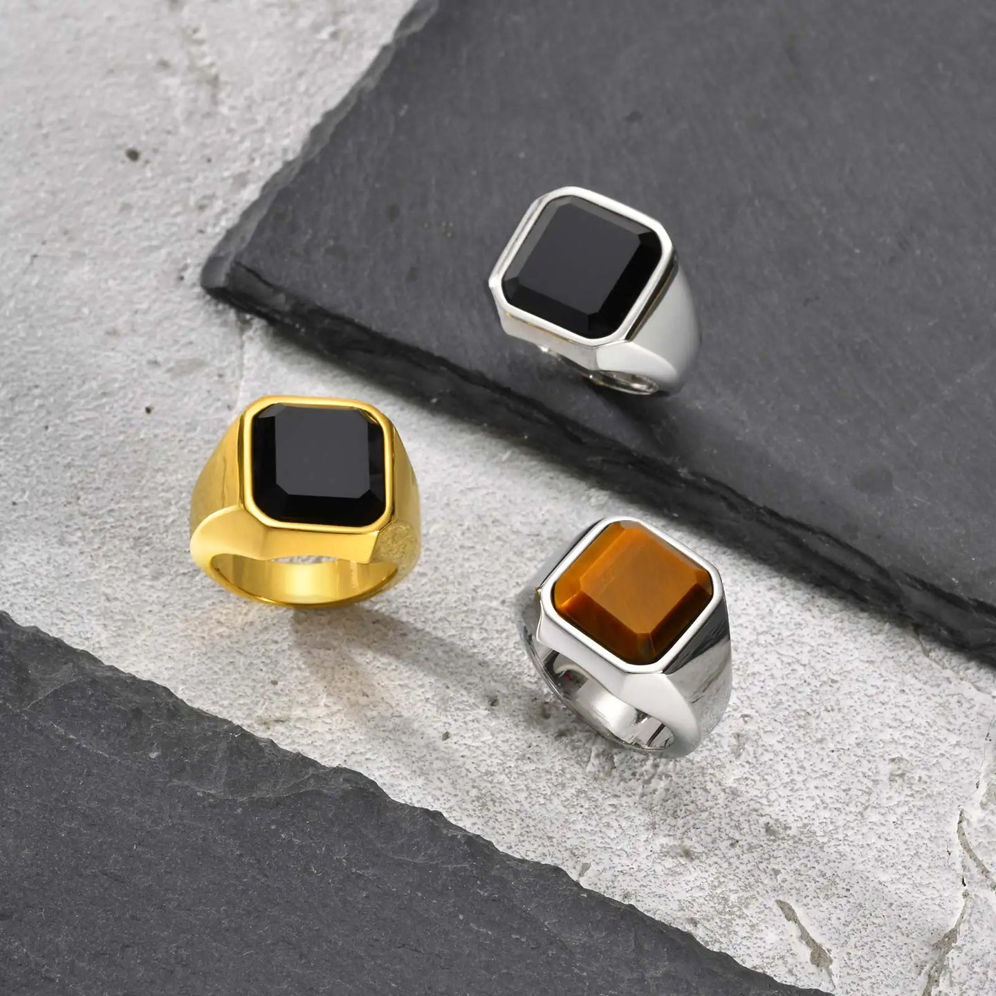 Three rings with square gemstones on a stone surface