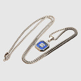Silver necklace with a blue and black pendant on a wooden surface