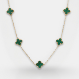 Gold necklace with green gemstone clover pendants on a light gray background