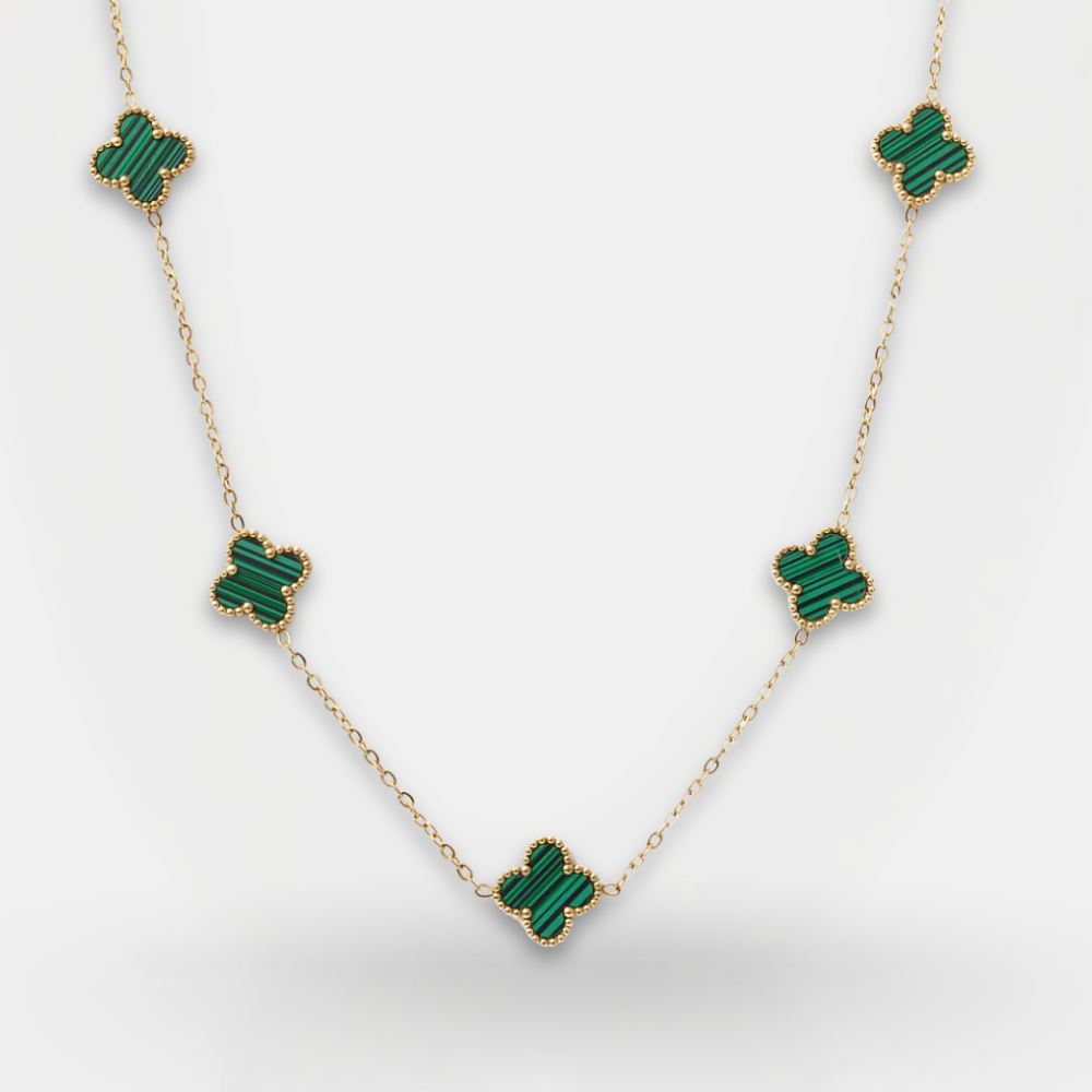 Gold necklace with green gemstone clover pendants on a light gray background