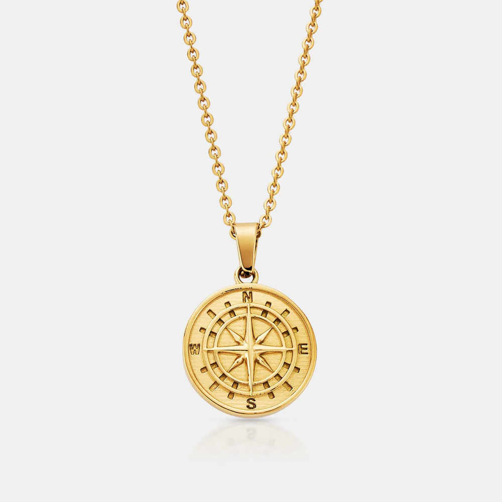 Gold compass necklace on a light gray background