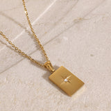 Gold necklace with a square pendant on a light stone surface