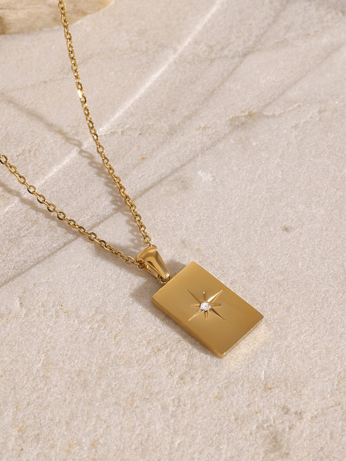 Gold necklace with a square pendant on a light stone surface