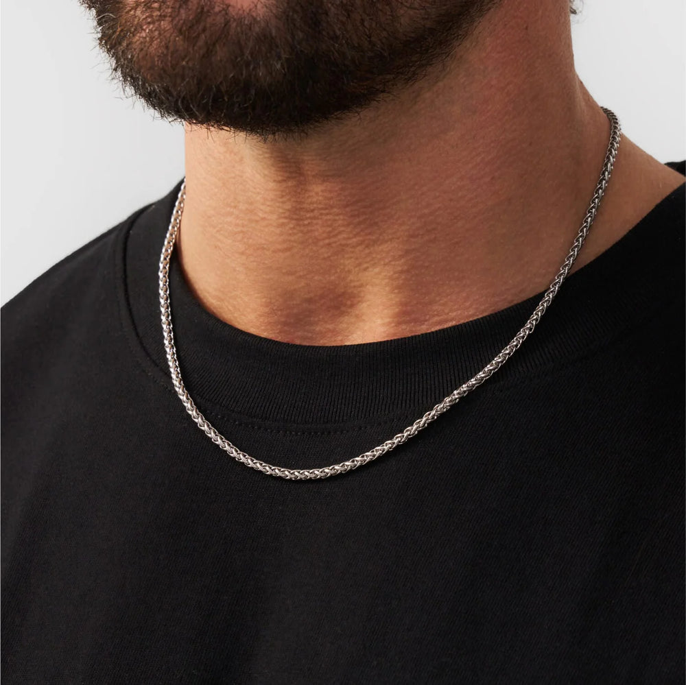 Man wearing a silver chain necklace against a plain background