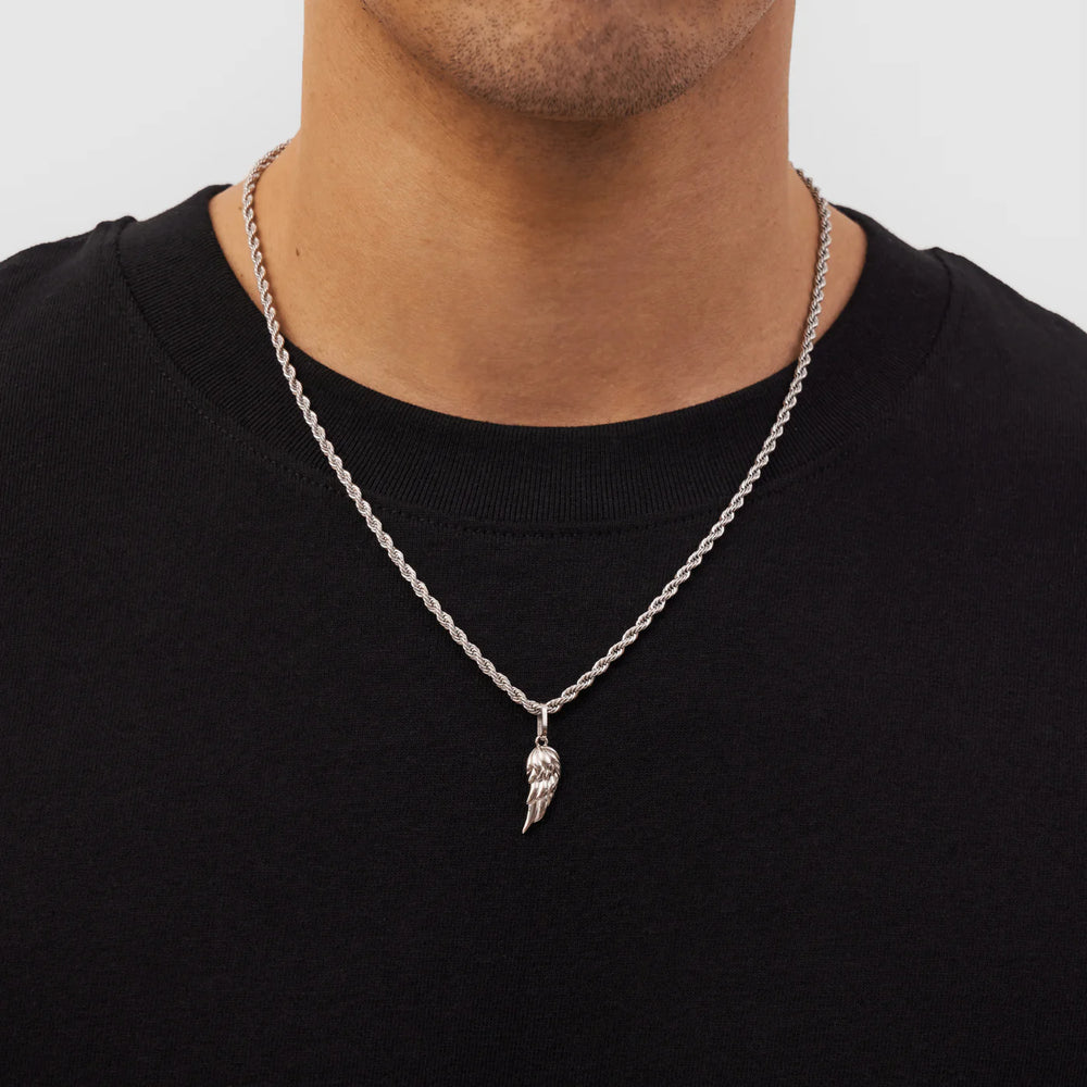 Silver chain necklace with a wing pendant worn by a person on a plain background