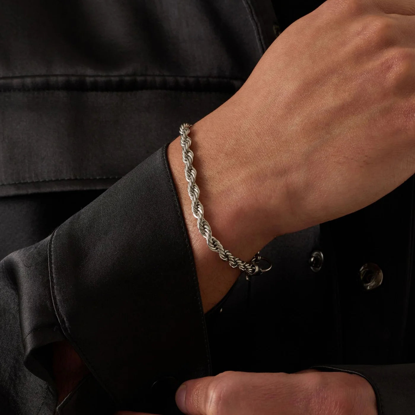 Silver chain bracelet on a person's wrist with a dark jacket background